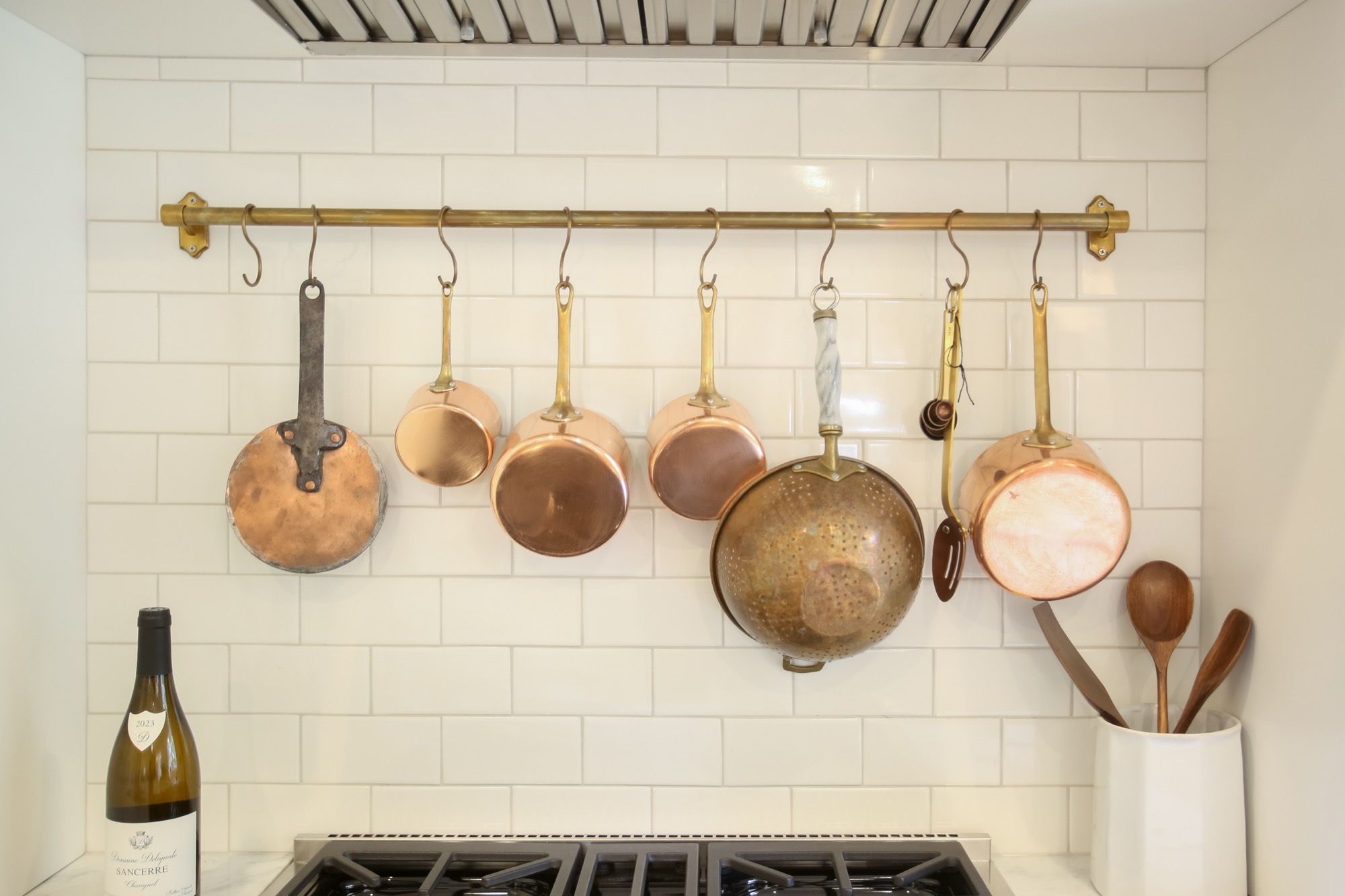 Copper pots on a brass rail over white subway tile